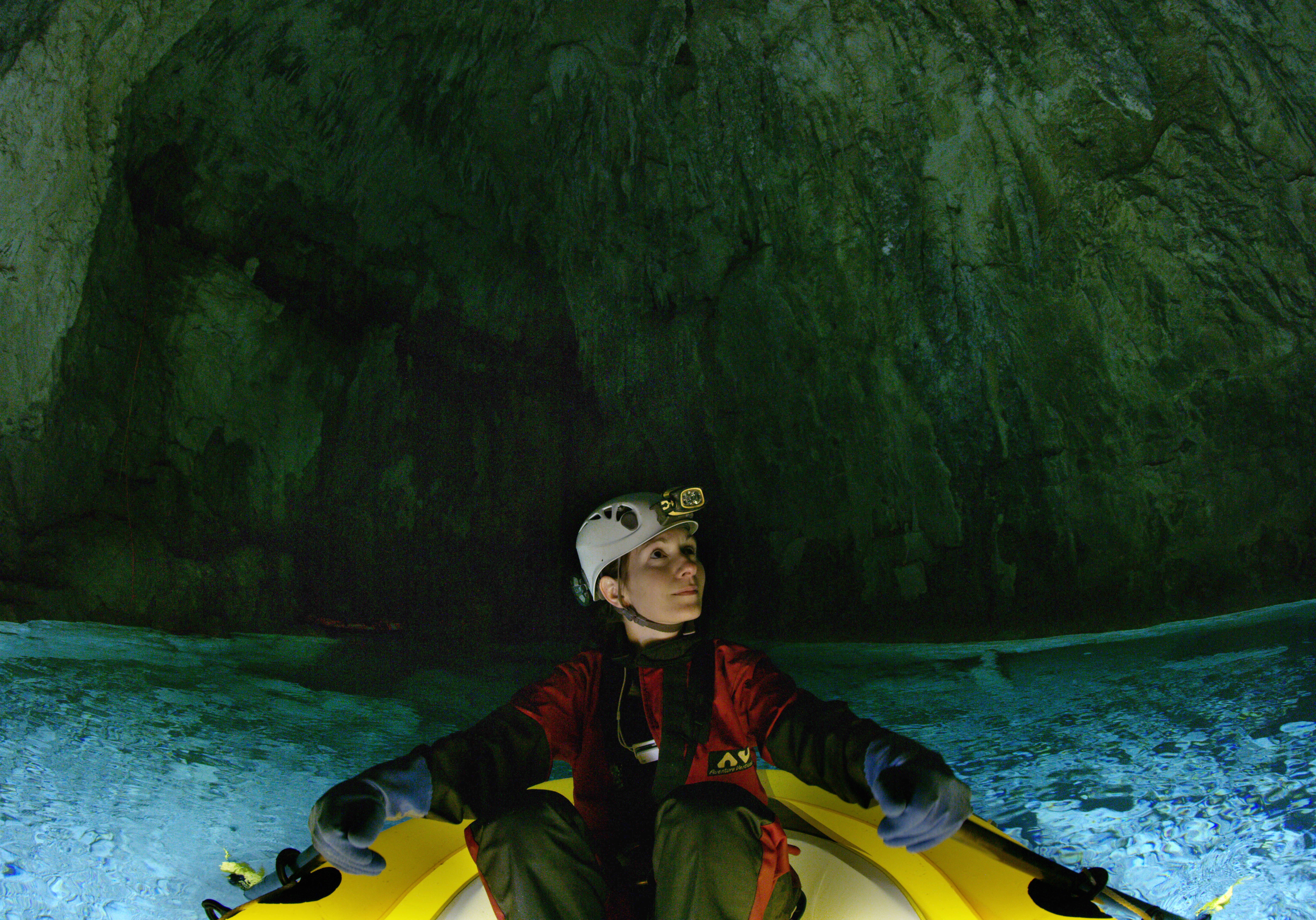 Person on a raft inside of a cave looking to their left surrounded by blue water.