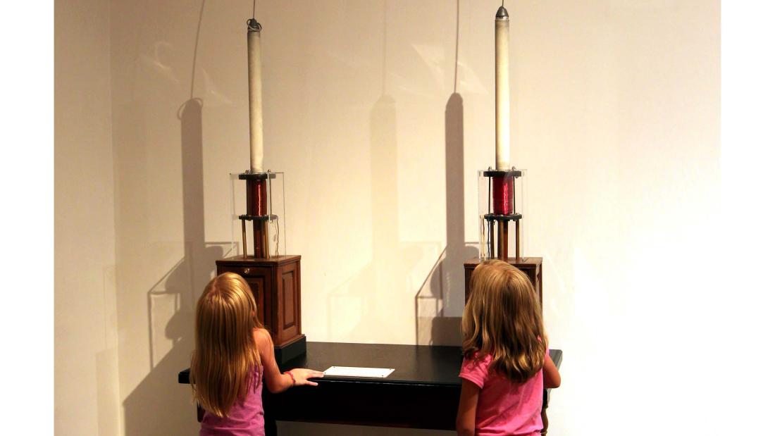 Two young strawberry blonde girls look up at an electricity display on a wall at the Fleet Science Center