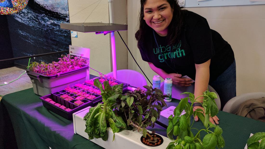 A woman stands leaning over a table with a display of green plants and uv lights