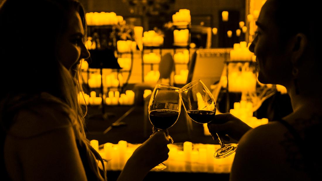 Two women clinking wine glasses in front of a room full of candles