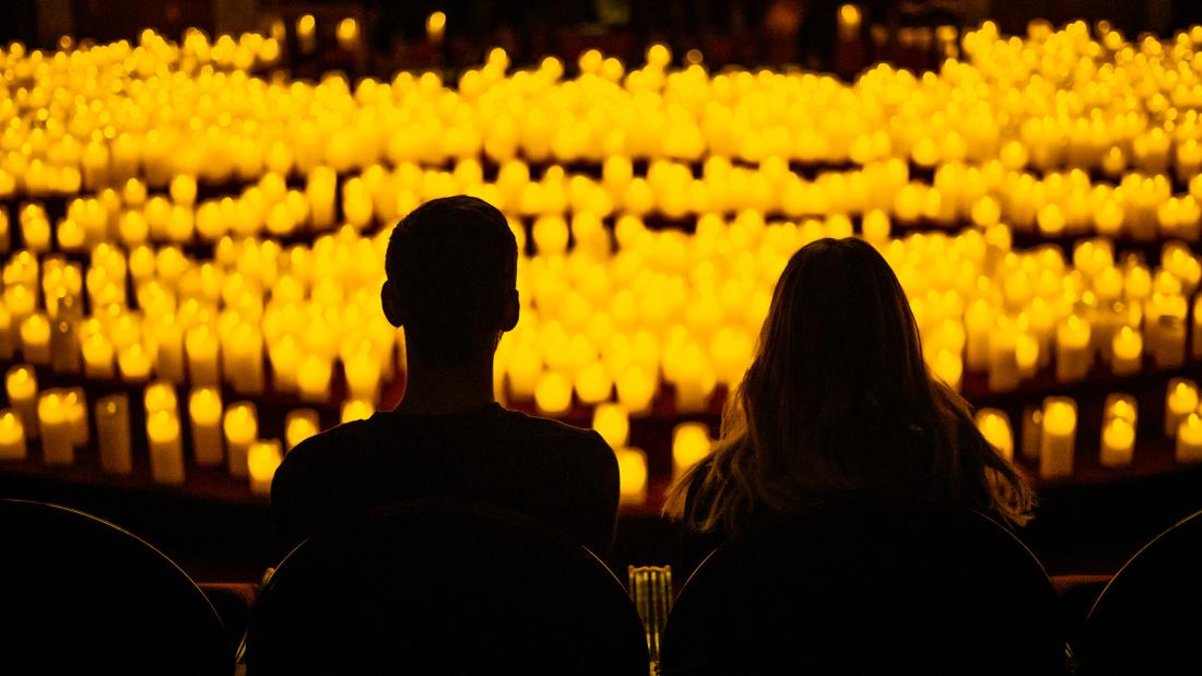 Two people from behind in darkness looking out over a room full of hundreds of candles