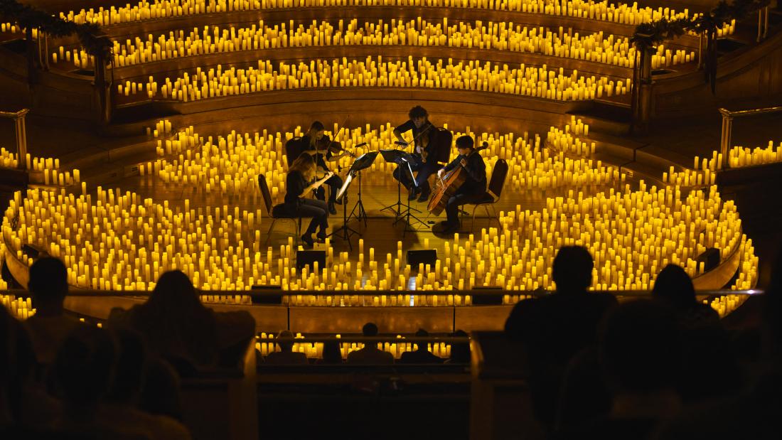A crowd looks down on a quartet of string musicians surrounded by hundreds of candles