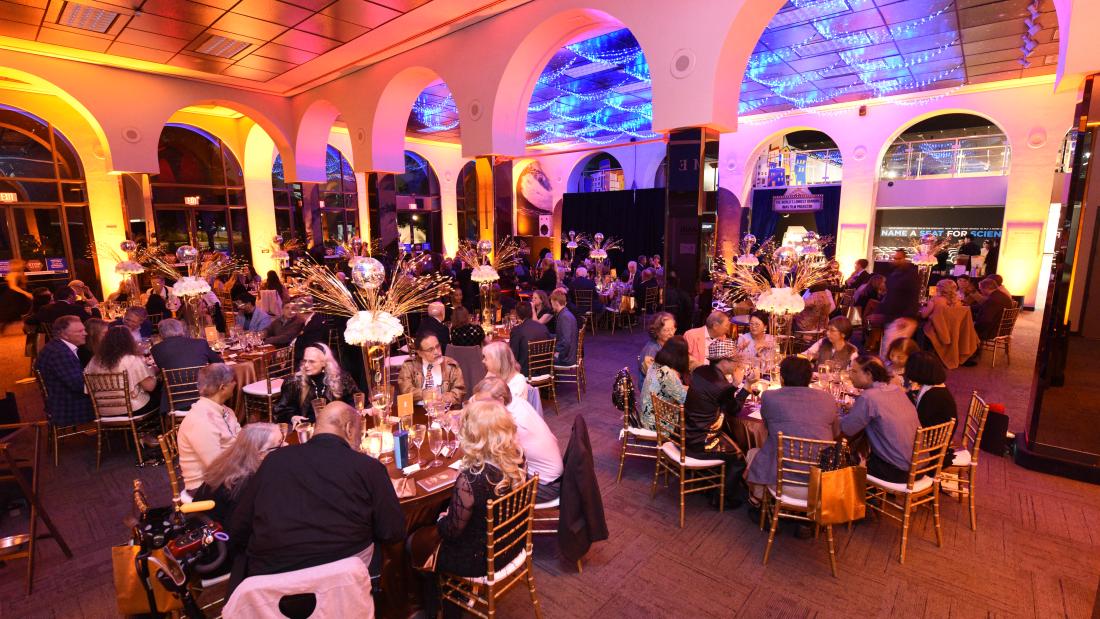 A wide image of a room lit in orange with people sitting at gala tables