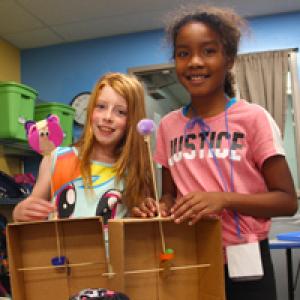 Two elementary-aged school girls smiling at the camera enjoying a science-based camp activity