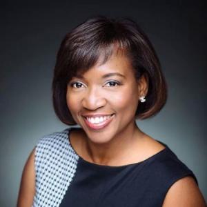 A black woman with short hair dressed in business-wear smiling at the camera 