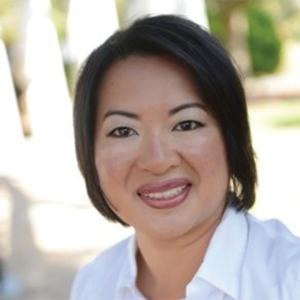 A middle aged asian woman with short dark hair in a white collared shirt smiling outside 