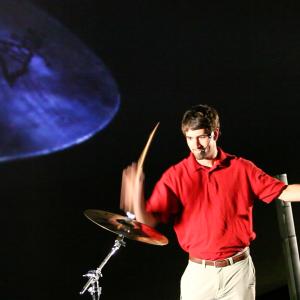 A man in a red shirt in action hitting a symbol with a drumstick