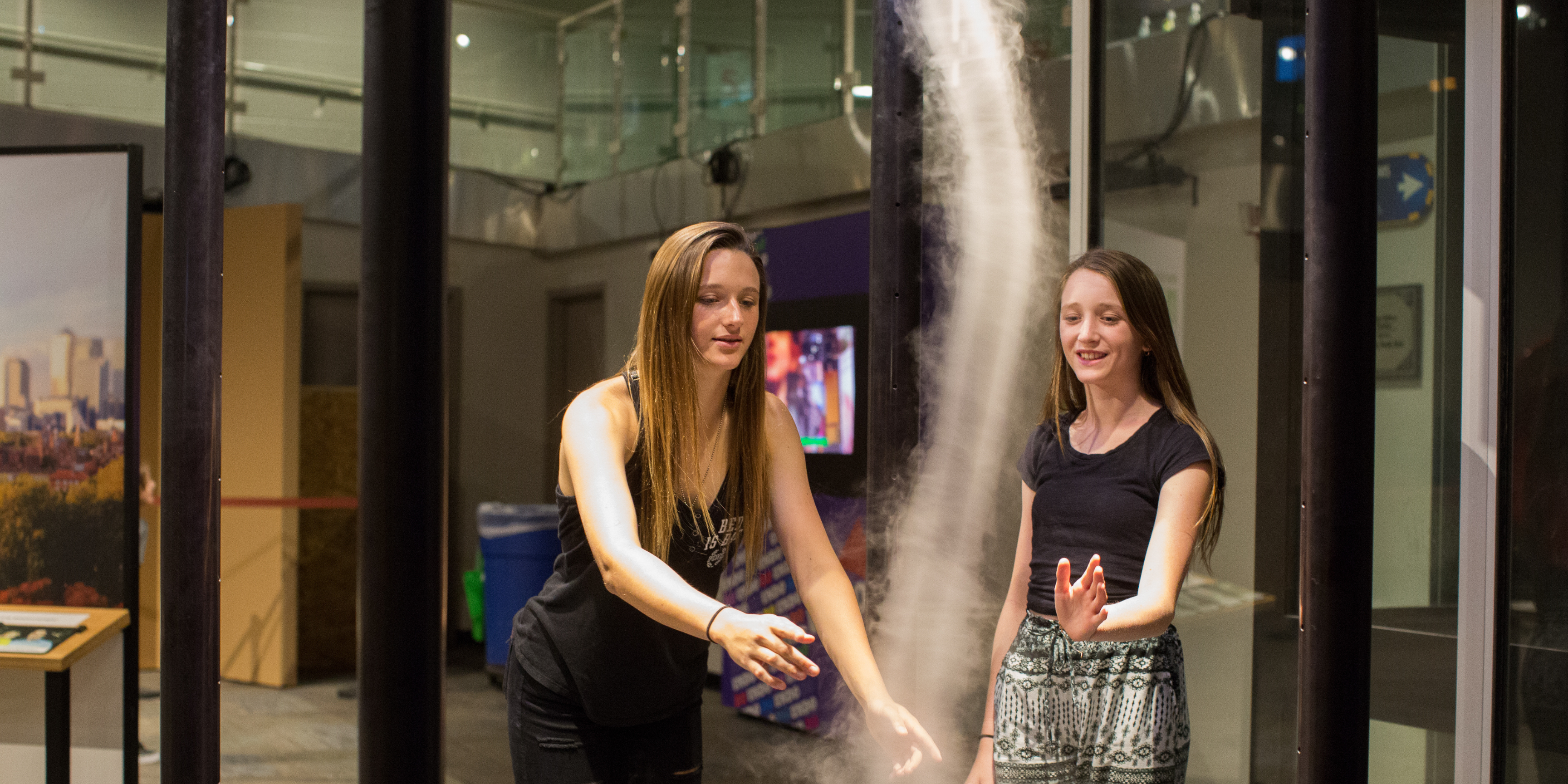 Two young adults moving their hands through the Tornado interactive at the Fleet Science Center