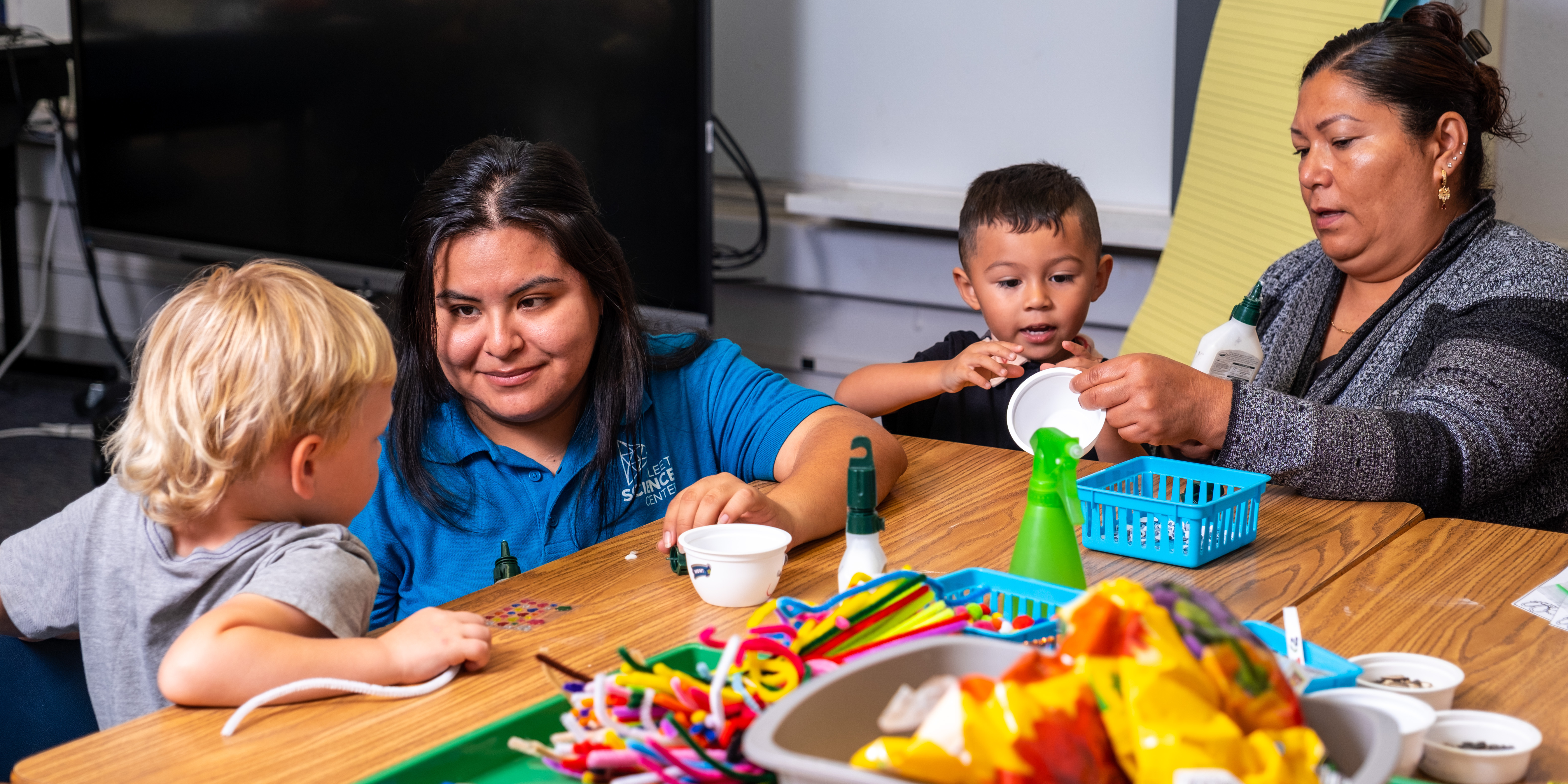 Sanchez Cruz encourages inquiry with Southeastern San Diegans at Encanto Elementary. Fleet educator and parent engaging in hands-on STEM learning with two young students inside of a classroom.