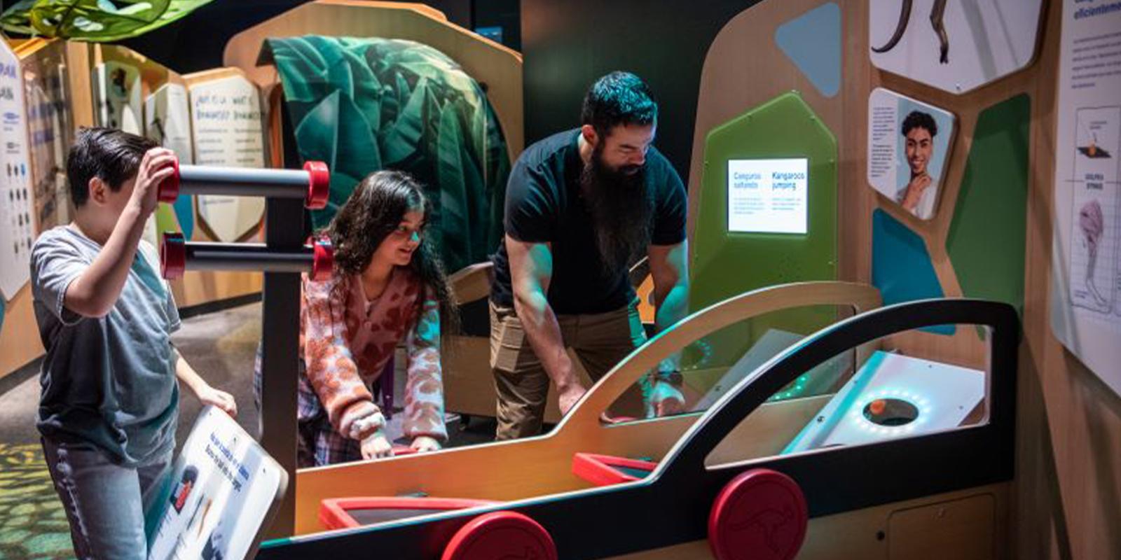A boy looks at a woman and man interacting with a science exhibit shaped like a car