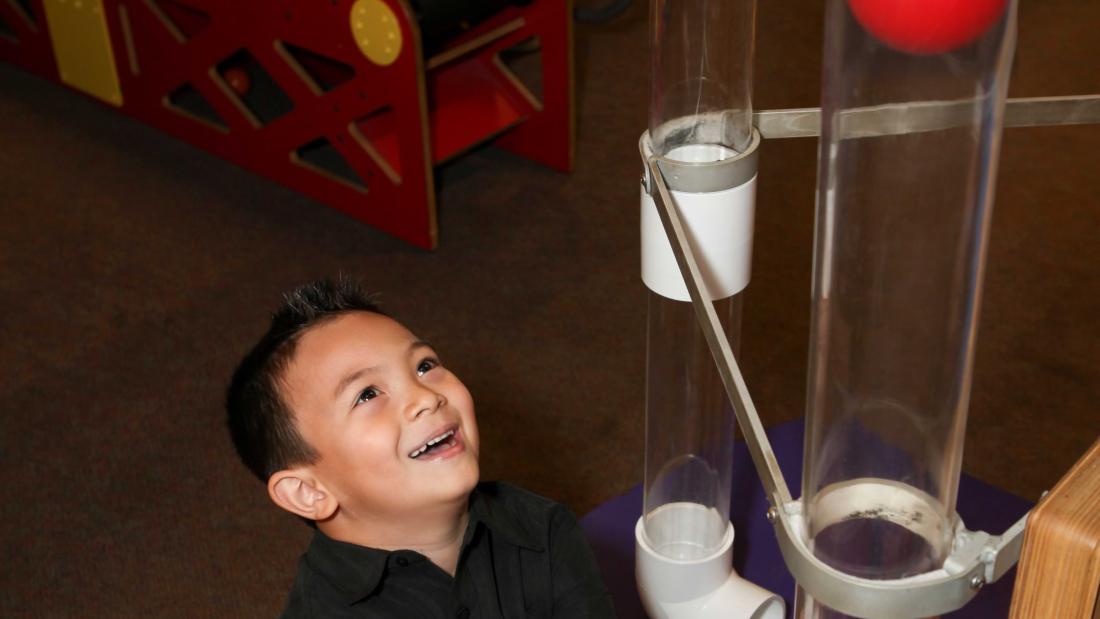 A young Filipino boy plays with a red ball in a pneumatic tube at the Fleet Science Center