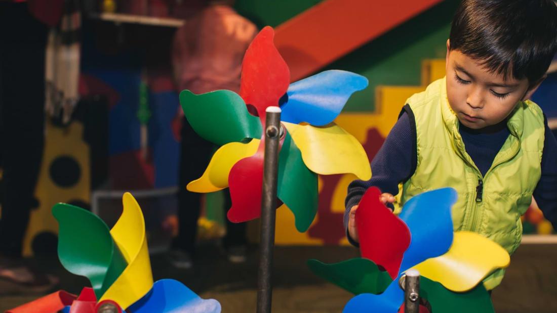A young hispanic boy in a green puffy vest plays with colorful pinwheels at the Fleet Science Center