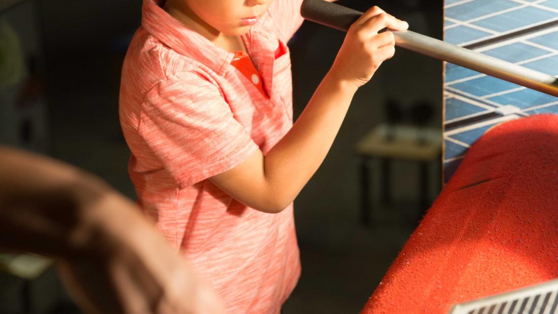 A young boy focuses very hard on an exhibit will pressing a button and maneuvering a lever at the Fleet Science Center