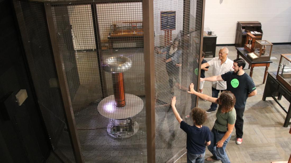 Group of people touching a cage surrounding a tesla coil at the Fleet Science Center