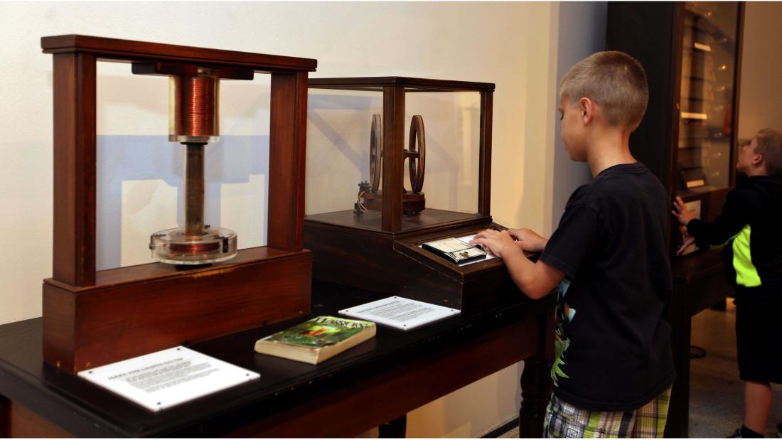 Young blonde boy experimenting with an old fashioned electrical device surrounded by wood and glass at the Fleet Science Center