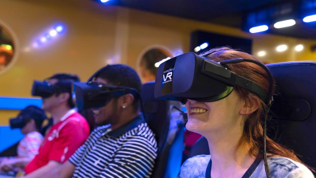 A young woman sits in a row of people all wearing VR headsets while smiling at the Fleet Science Center