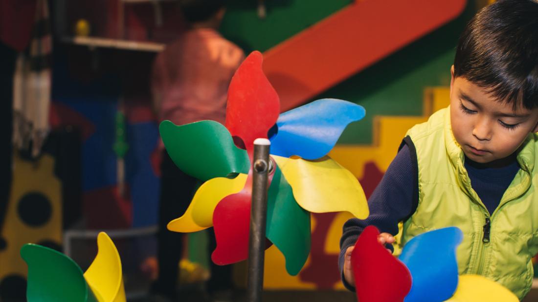 Young boy playing with rainbow pinwheels.