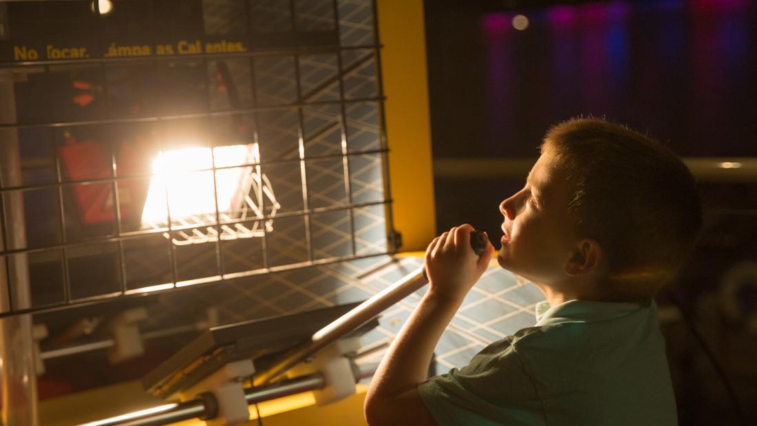 A young boy pulls a lever in front of a metal grate and is illuminated by a bright bulb