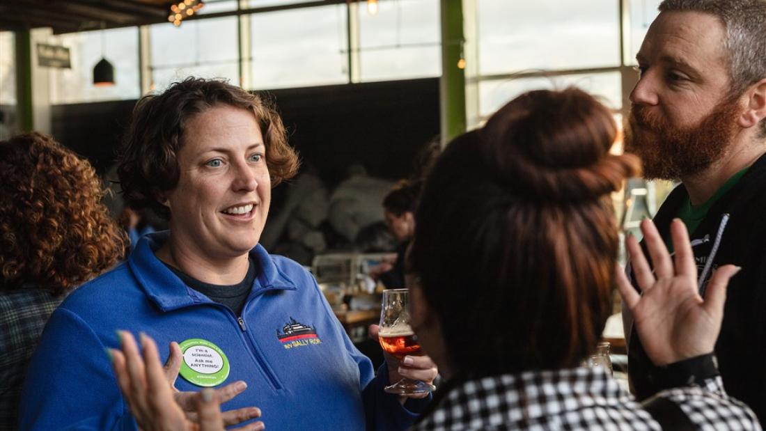 A woman talks to a man and woman in a brewery