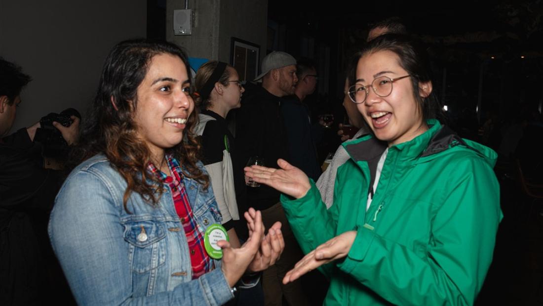 Two women smile and laugh in a darkened brewery