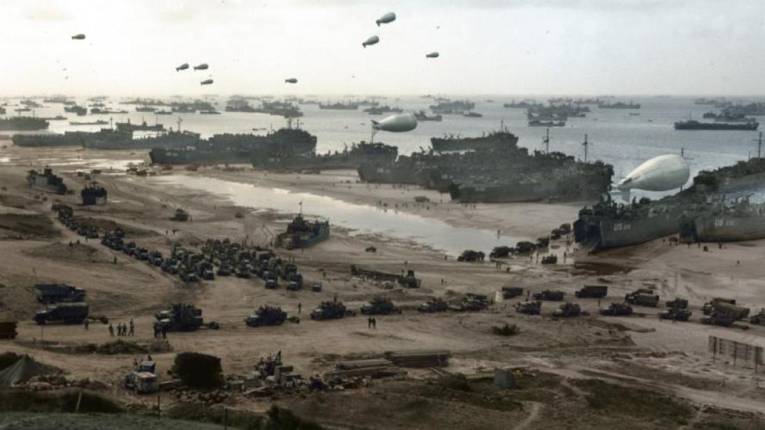 Many tanks and trucks sit along the coast in the water and drive across the beach.