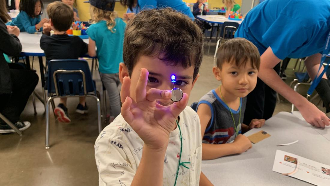 Young child holding up a lit circuit and lightbulb.