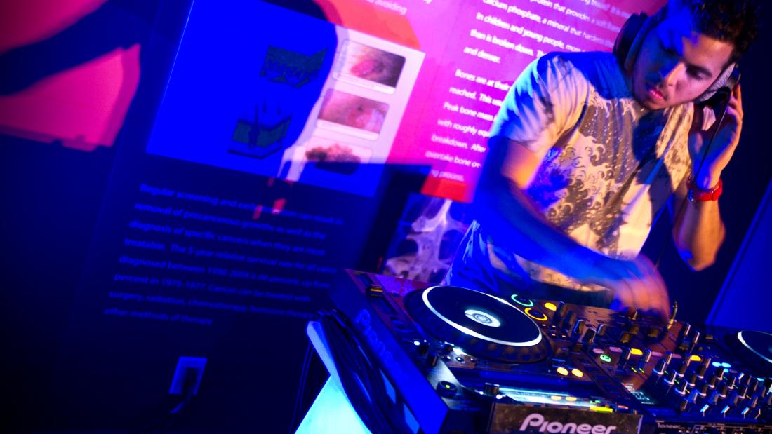 A DJ in a spotlight with exhibit wall text behind him.