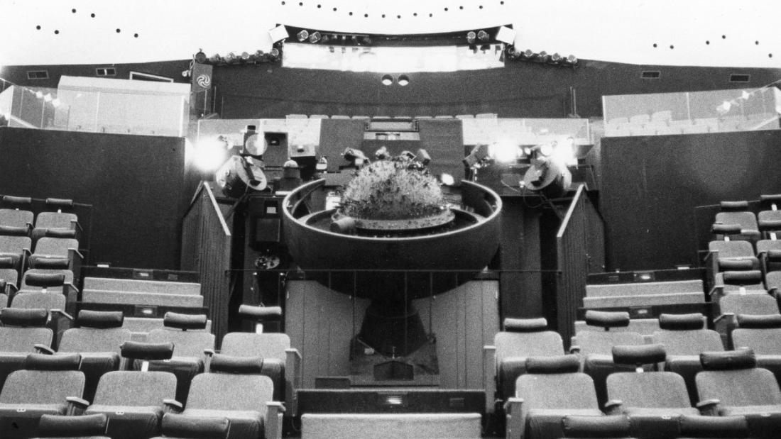 Black and white image of the round star projector in the center of a theater with rows of chairs  