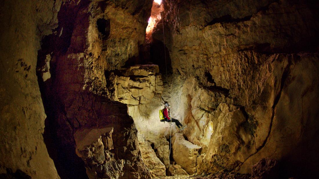 A cave diver lowering themselves into a large cave.