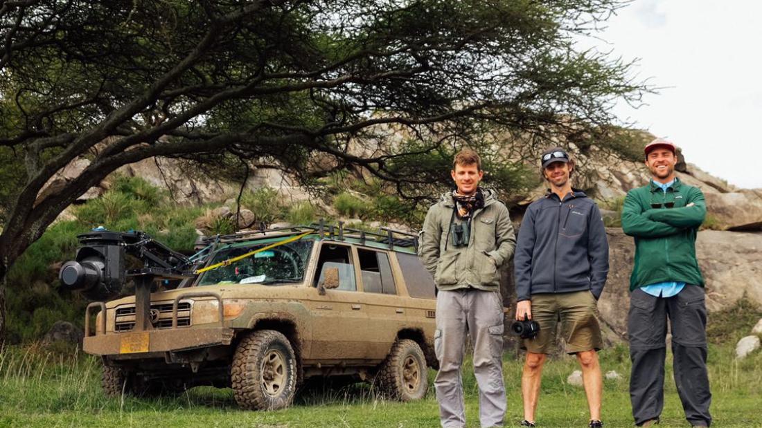 Three white men stand in front of a very muddy jeep under a tree
