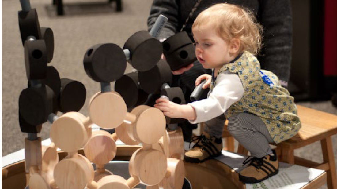 A toddler girl crouching on a table playing with magnetic circle blocks.