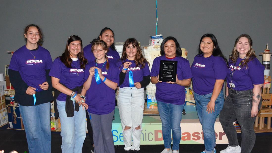 Group of young women and a female teacher in purple shirts pose at the SciTech Challenge competition
