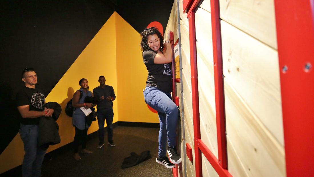 Woman in jeans climbs a wall at a museum exhibit