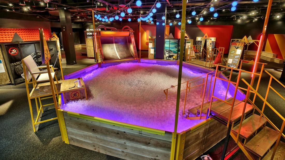 An octagonal above ground pool made out of wood filled with white balls and purple lighting on them
