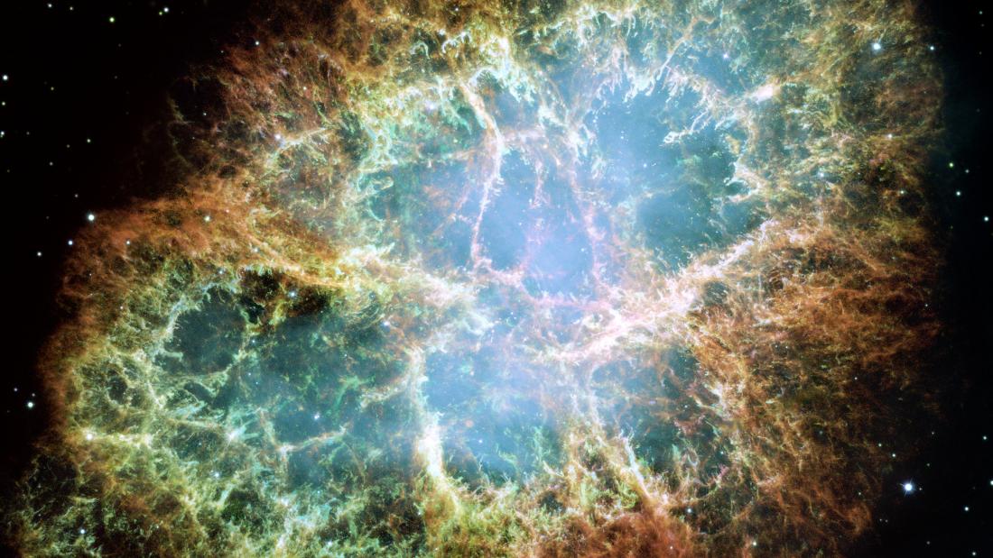 The Crab Nebula with yellow and orange colors on the circular rim that branch and crackle into the center which is more blue