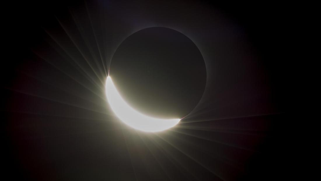 A total solar eclipse with only one quarter of the sun still shining from behind a black circle moon