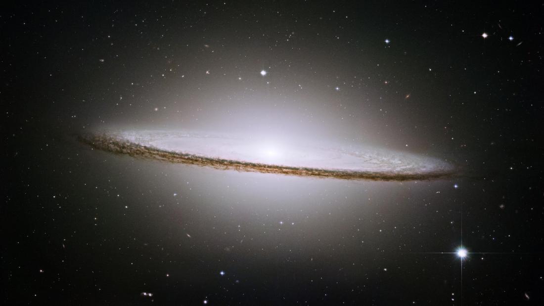 A white galaxy glowing against the dark shaped like the brim of a sombrero