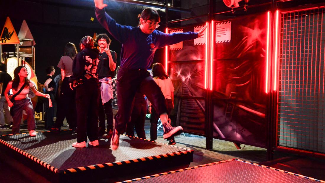 Group of young people laughing and jumping on metal plates with red lights shining at the side. 