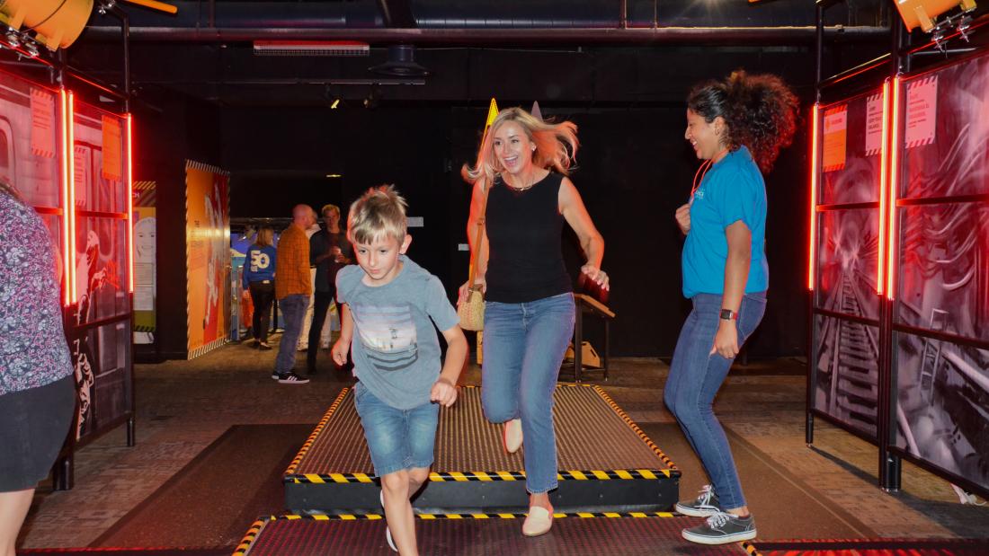 The Worst-Case Scenario visitors can develop essential survival skills with interactive, immersive experiences. Blonde woman and blonde male child run forward as brunette woman watches