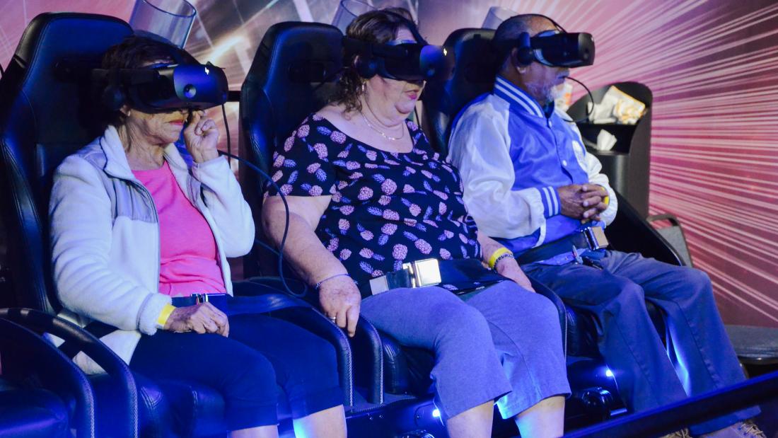 Three older adults ride in a VR experience while wearing VR headsets
