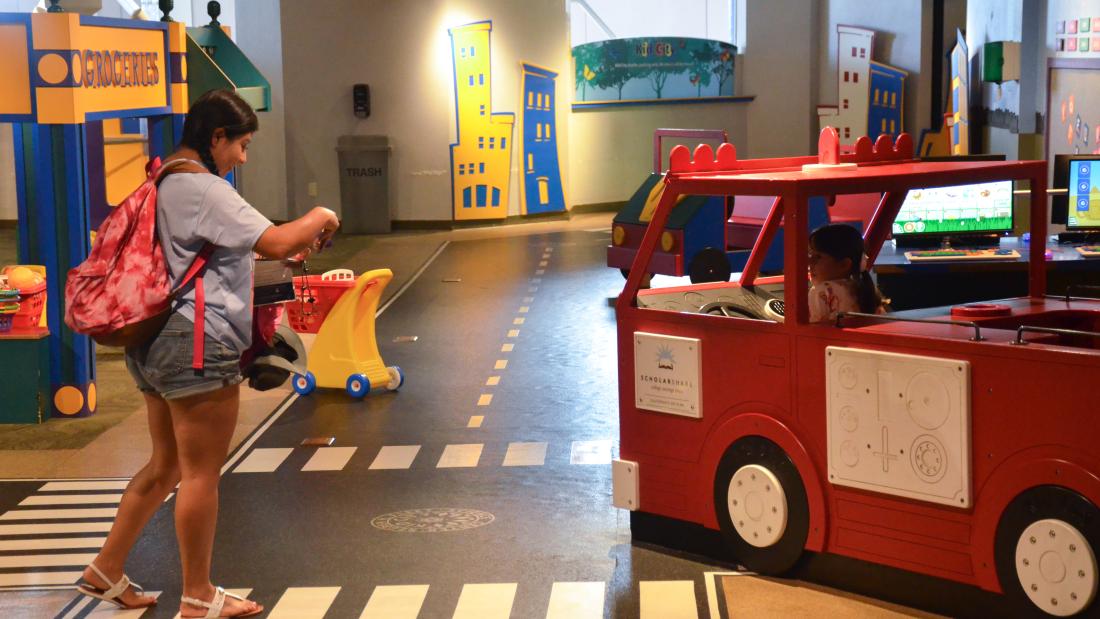A woman takes a photo of a child playing in a miniature firetruck