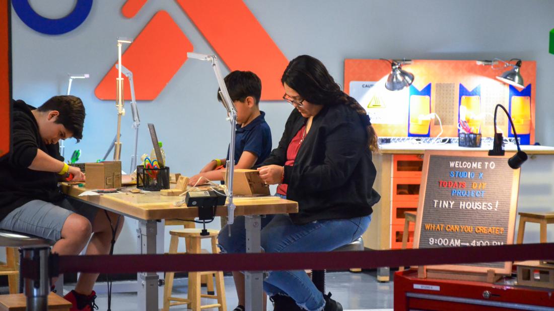 The Fleet brings communities to the science center with Community Mornings. Adult woman and two male teens working at a table with tools