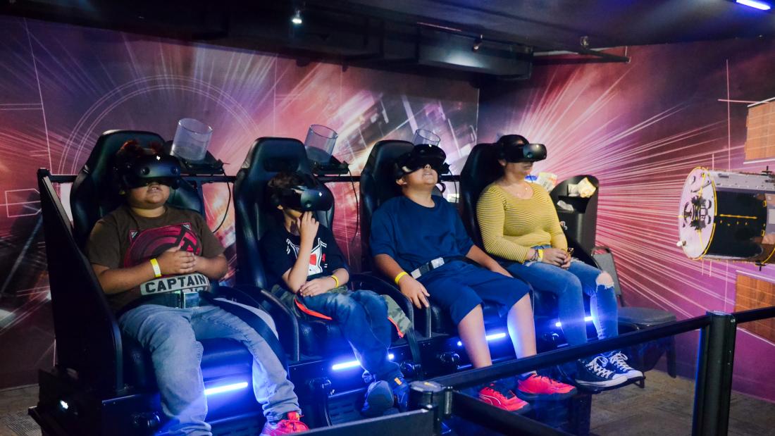 A group of four people sit in a VR experience while wearing VR headsets