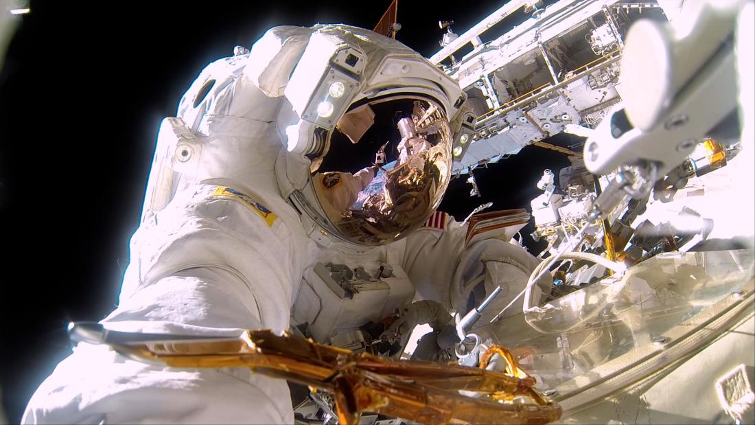 An astronaut wearing a full suit and helmet outside of the ISS taking a selfie.