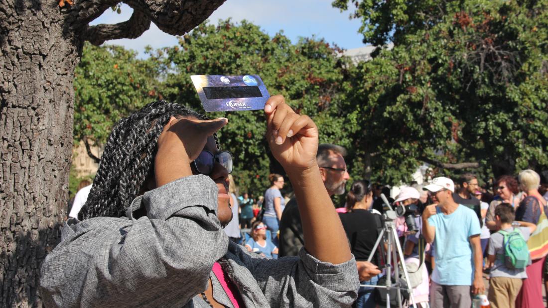 A woman holds a viewer up to the sky and squints through to watch an eclipse