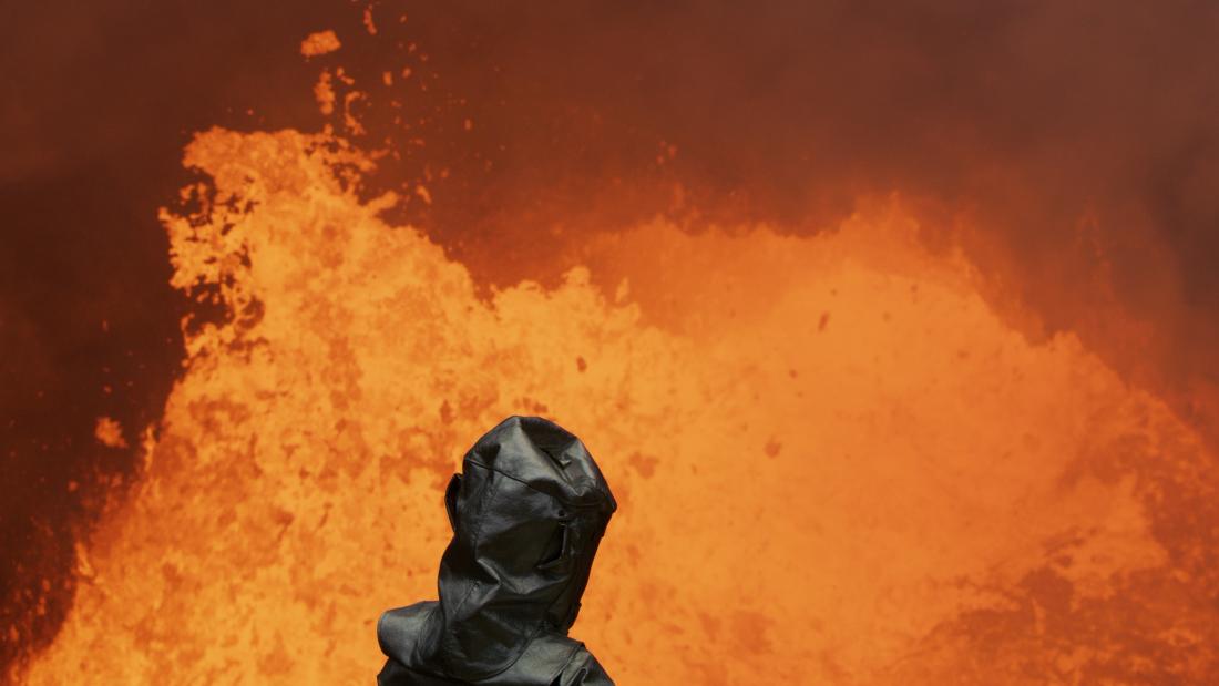 A person from behind standing in front of a spout of lava