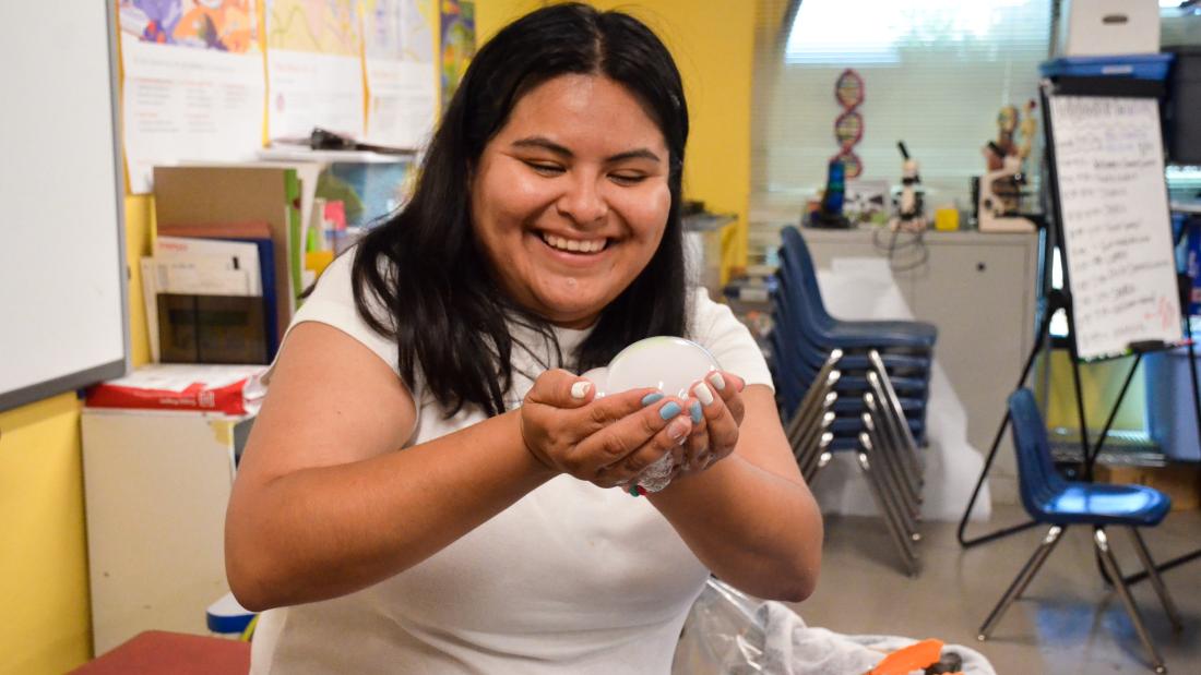 Fleet Science educator shares the joy of science Young woman with shoulder-length dark brown hair smiling and holding a ball of foam