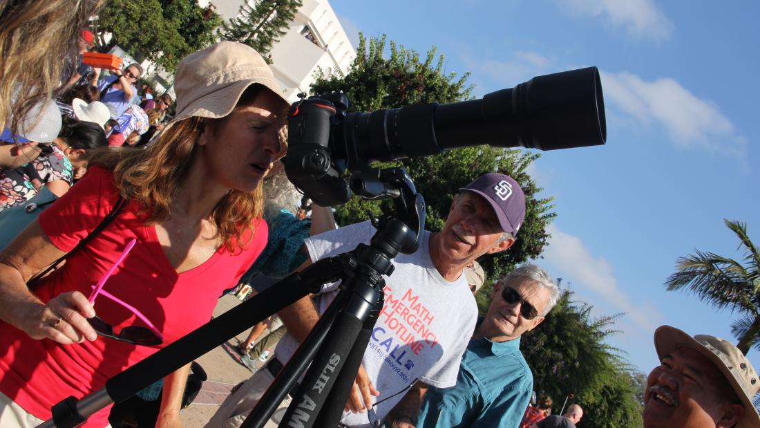 A woman looks up through a telescope while two men watch
