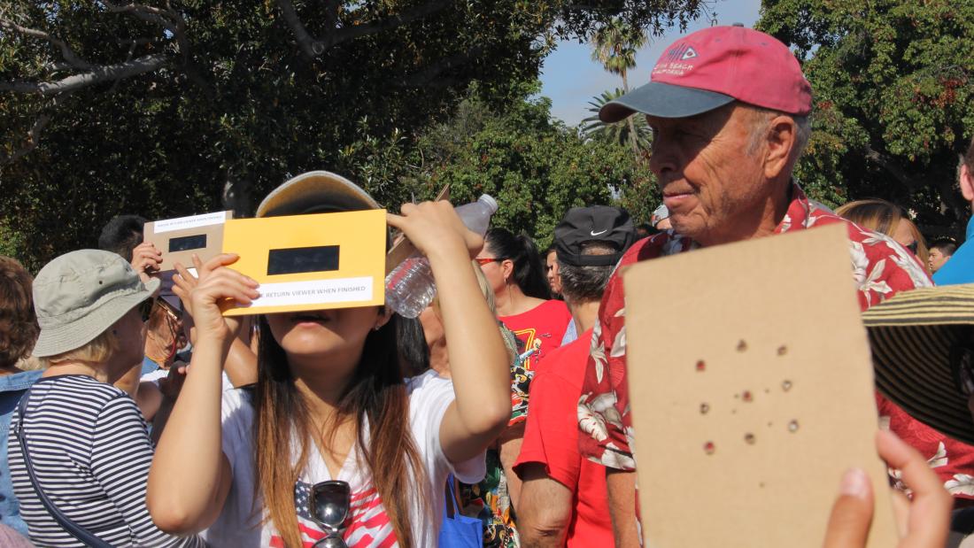A young girl holds an eclipse filter to her face while a man looks on