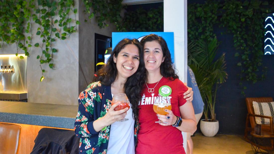 Two women pose with arms around each other and drinks in hand